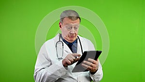 Senior doctor in white coat reads something on tablet, not understand anything.