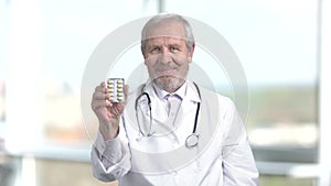 Senior doctor in white uniform showing pills.