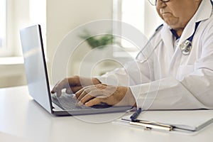 Senior doctor using laptop, giving online consultations to patients or entering data into system