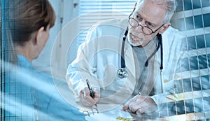 Senior doctor writing prescription to his patient; light effect; multiple exposure