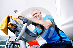 Senior doing sport on spinning bike in gym