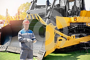 Senior driver engineer in hardhat is using tablet computer in construction site background bulldozer