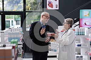 Senior drugstore employee helping elderly customer with cardiology medications explaining medical leaflet