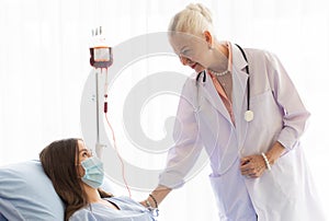 The senior elder female doctor visits the ward and talks to a patient on a bed for diagnosis and curing