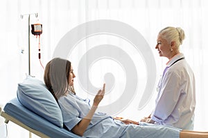 The senior elder female doctor visits the ward and talks to a patient on a bed for diagnosis and curing