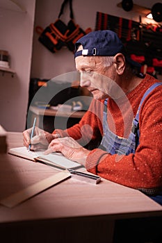 Senior elderly Carpenter writing project notes in woodwork workshop. Profession and small business concept