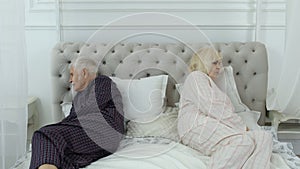 Senior elderly couple in pyjamas lying on bed having an argument in bedroom. Grandparents quarrel