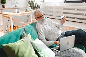 Senior elderly man making online payments using laptop. Old grandfather doing shopping ecommerce with credit card