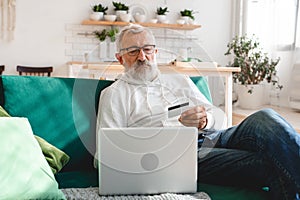 Senior elderly man making online payments using laptop. Old grandfather doing shopping ecommerce with credit card