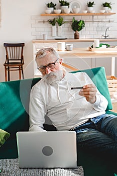 Senior elderly man making online payments using laptop. Old grandfather doing shopping ecommerce with credit card