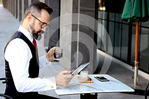 Senior elderly mature business man using digital table during having a coffee at outdoor cafe, happy people taking a break from