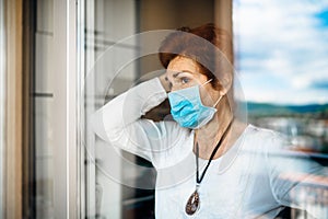 Senior elderly sad woman at home looking through the window.Coronavirus COVID-19 disease outbreak infection risk.Lockdown