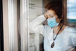 Senior elderly sad woman at home looking through the window.Coronavirus COVID-19 disease outbreak infection risk.Lockdown