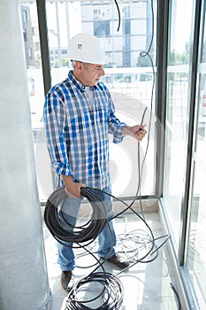 senior electrician holding reel cable at indoor work site