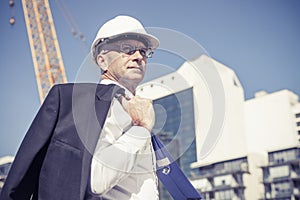 Senior elegant builder man in suit at construction site on sunny