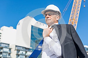 Senior elegant builder man in suit at construction site on sunny summer day