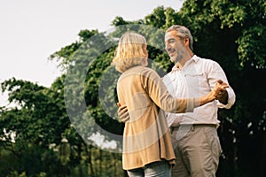 Senior elegant caucasian couple dancing looking at each other feeling love and cherish on their anniversary in the park with copy