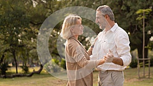 Senior elegant caucasian couple dancing looking at each other feeling love and cherish on their anniversary in the park with copy