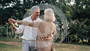 Senior elegant caucasian couple dancing looking at each other feeling love and cherish on their anniversary in the park with copy