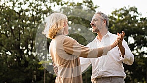 Senior elegant caucasian couple dancing looking at each other feeling love and cherish on their anniversary in the park with copy