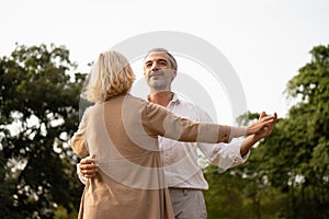 Senior elegant caucasian couple dancing looking at each other feeling love and cherish on their anniversary in the park with copy