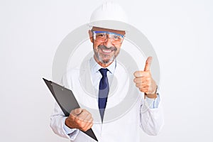 Senior engineer man wearing helmet glasses holding clipboard over isolated white background happy with big smile doing ok sign,