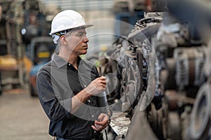 Senior engineer using laptop computer checking list old used car engine in machinery parts shop warehouse. old technician man