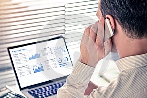 Senior executive manager analysing a financial report on computer in office and calling on the phone, working with operations data