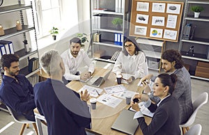 Employees listening to senior executive sitting around office table in corporate meeting