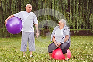 Senior exercise - Happy senior couple sitting on fitness balls in park