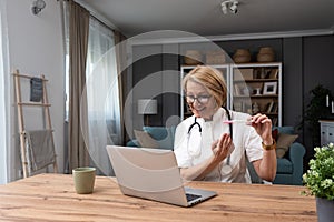 Senior experienced female doctor showing pregnancy test in online video call on laptop while sitting in home office from private