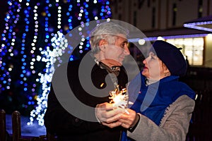 Senior family couple burning sparklers by holiday illumination at night