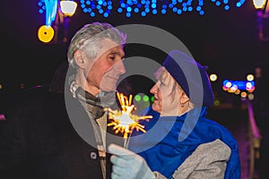 Senior family couple burning sparklers by holiday illumination at night