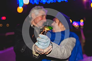 Senior family couple burning sparklers by holiday illumination at night. Close up