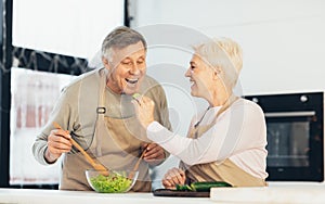 Senior Family Couple Feeding Each Other Cooking Dinner In Kitchen