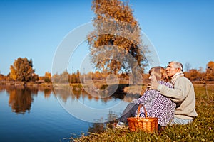 Senior family couple having picnic by autumn lake. Happy man and woman enjoying nature and hugging
