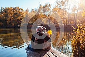 Senior family couple relaxing by autumn lake. Man and woman enjoying nature and hugging sitting on pier