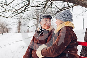 Senior family couple sitting on bench outdoors during snowy winter weather. Elderly people chatting. Valentine's day