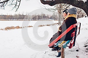 Senior family couple sitting on bench outdoors during snowy winter weather. Elderly people enjoy landscape. Space