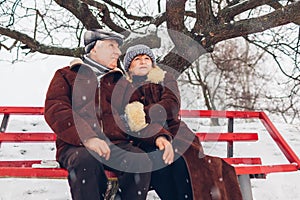 Senior family couple sitting on bench outdoors during snowy winter weather. Elderly people. Valentine& x27;s day
