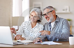 Senior family couple studying online together at home, looking at laptop while sitting at table