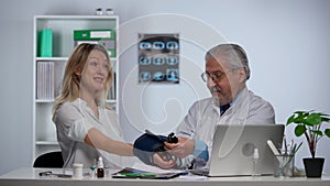 Senior family doctor measures blood pressure with a tonometer to woman patient and speaking to her during consultation