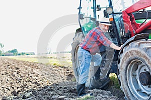 Senior farmer hopping in to drive tractor at field