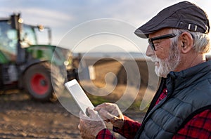 Senior farmer with tablet in field with tractor in background