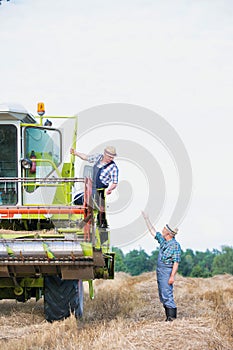 Senior farmer talking to mature farmer standing on harvester in field