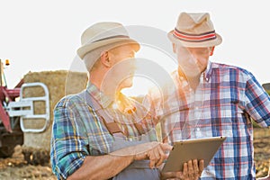 Close up of senior farmer using digital tablet with mature farmer standing against tractor in field photo