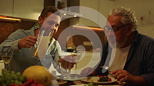 Senior father and adult son eating meal at table. Man pouring juice into glass