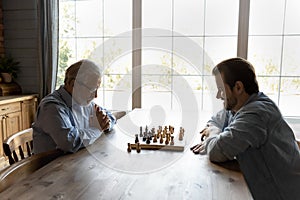 Senior father and adult son play chess at home