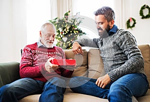 A senior father and adult son with a present sitting on a sofa at Christmas time.