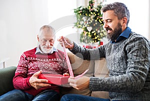 A senior father and adult son with a present sitting on a sofa at Christmas time.